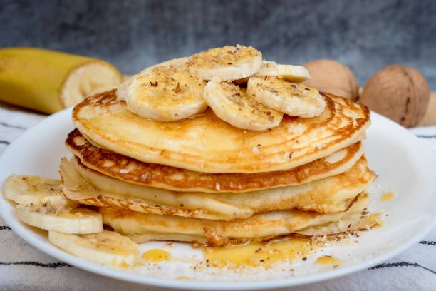 Homemade Vegan Banana pancakes topped with fresh banans, syrup and chopped walnuts.