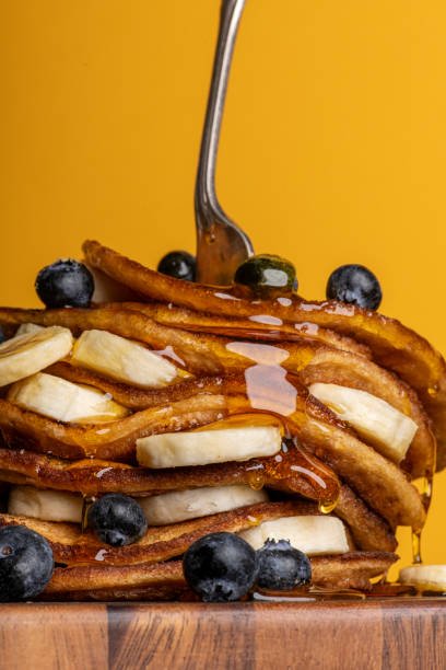 Delicious vegan banana pancakes stacked layered with banana and blueberries and covered with golden syrup.