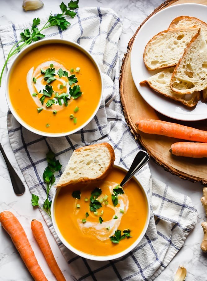 Delicious homemade 2 bowls of carrot and ginger soup served bread served topped with cream and cilantro.