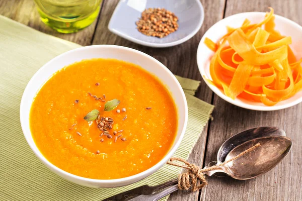 Homemade carrot and ginger soup served in a white bowl with fresh sliced carrot and spoon on a table