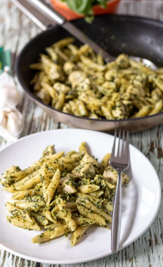 Easy homemade chicken pesto pasta served on a plate with a fork and skillet of pesto pasta in the background