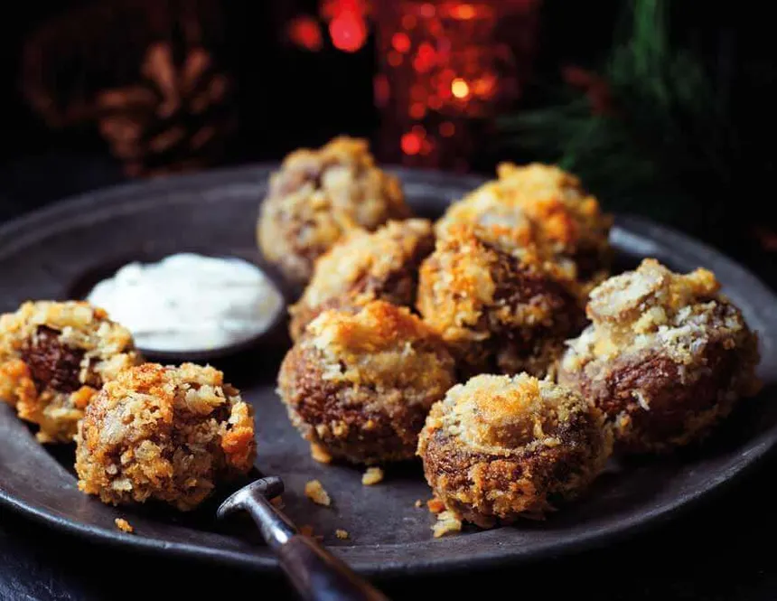 Easy crispy  homemade crumbed mushrooms served on a black plate with a dip.