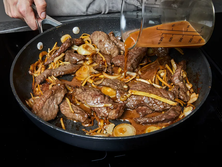 homemade beef onion stir fry in a pan with marinade poured into pan