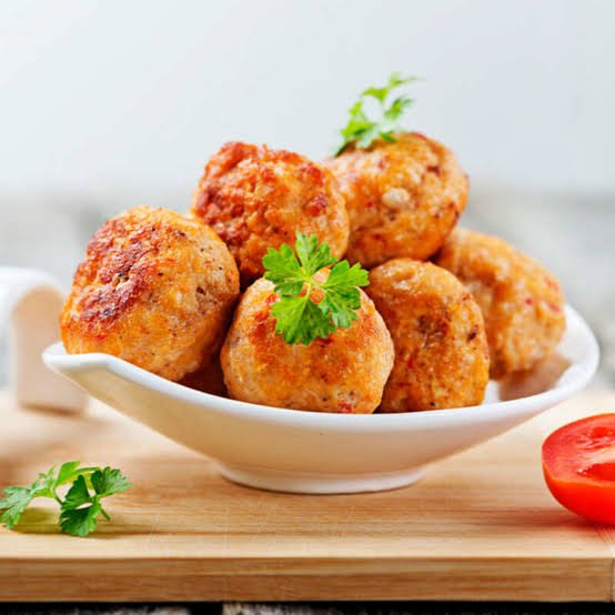 Homemade easy chicken meatballs with thats lightly crumbed. Garnished with parsley and served on a white plate on a serving board.