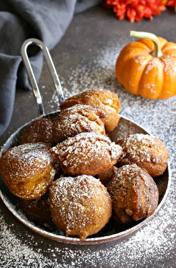 homemade pumpkin fritters in  a pan sprinkled with icing sugar