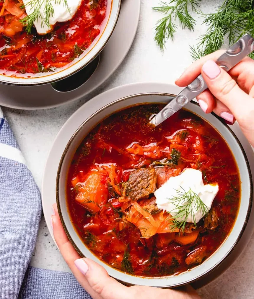 homemade borscht soup with beef and garnish with dill and sour cream in a round bowl served on a table
