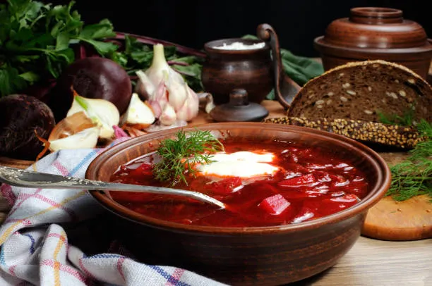 homemade borscht soup served with rye bread with fresh garlic and beetroot in the background