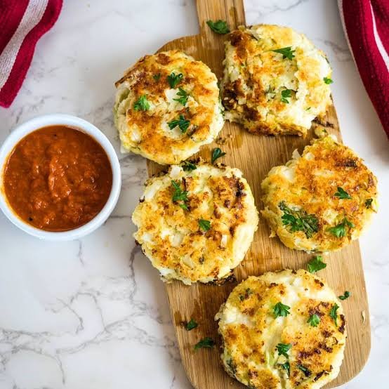 Crispy cabbage fritters served a wooden board with a salsa sauce on the side.