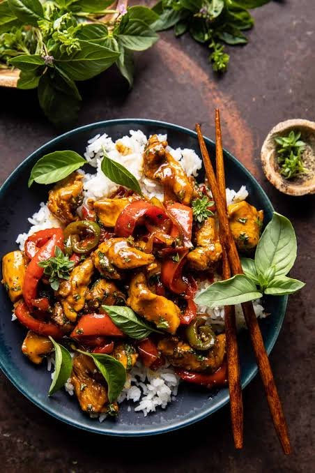 Quick chicken stir fry with fresh basil  and served with rice in a round blue bowl with chopsticks
