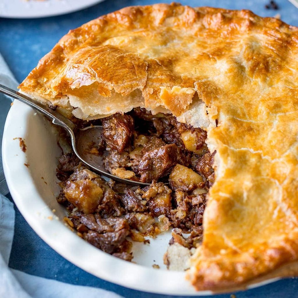 Easy homemade chunky beef pie  in a round white oven dish with spoon