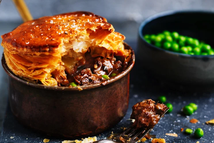 Individual serving size chunky beef pie with green peas on the side