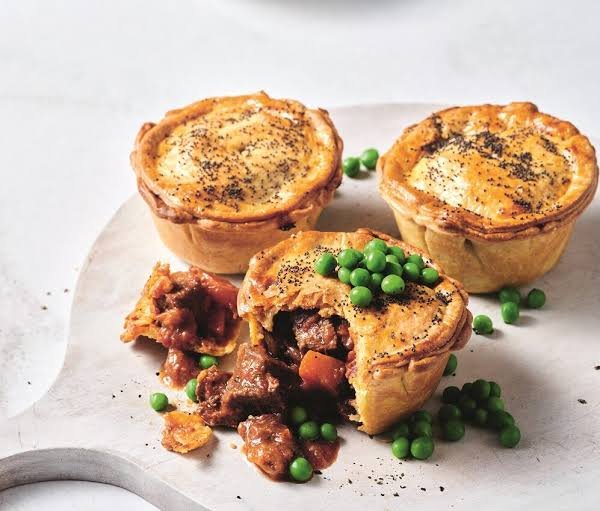 Three small chunky beef pie topped with pies and carrots served on a white board