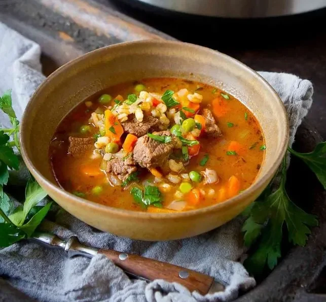 Instant pot beef barley soup in a bowl served on a table.