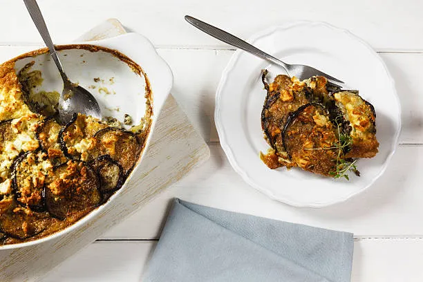 Delicious easy moussake recipe oven baked served on a white plate  on a table with grey napkin.