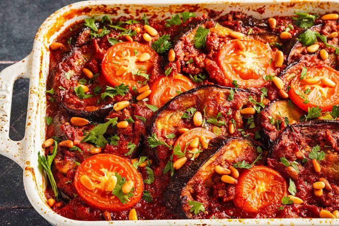 Easy moussaka recipe ready in minutes in a large white rectangular oven dish served on a table and topped with pine nuts.