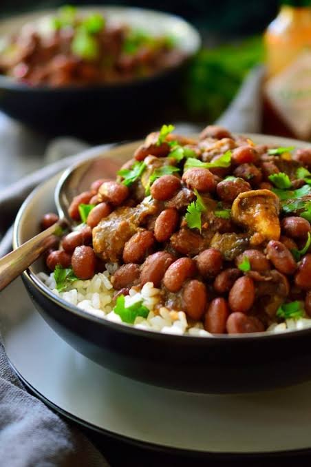 Homemade red beans rice with mushrooms served in a black round bowl on a table.