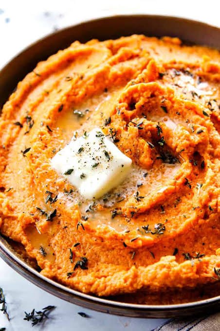 Homemade sweet potato mash with thyme and garlic in a round bowl topped with butter piece