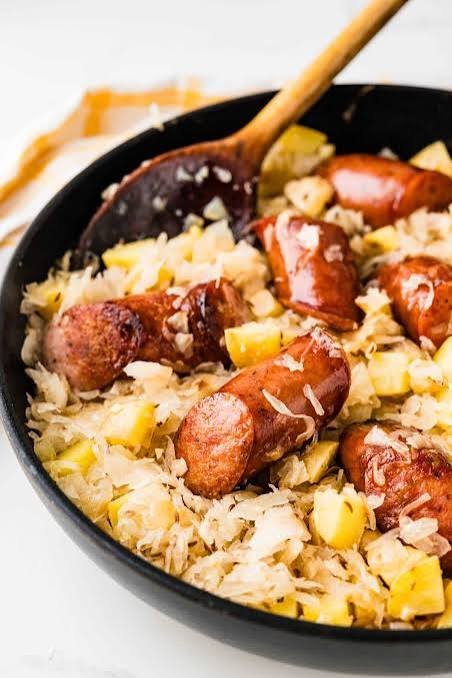 easy homemade one pot cabbage and sausage in a black skillet with wooden spoon